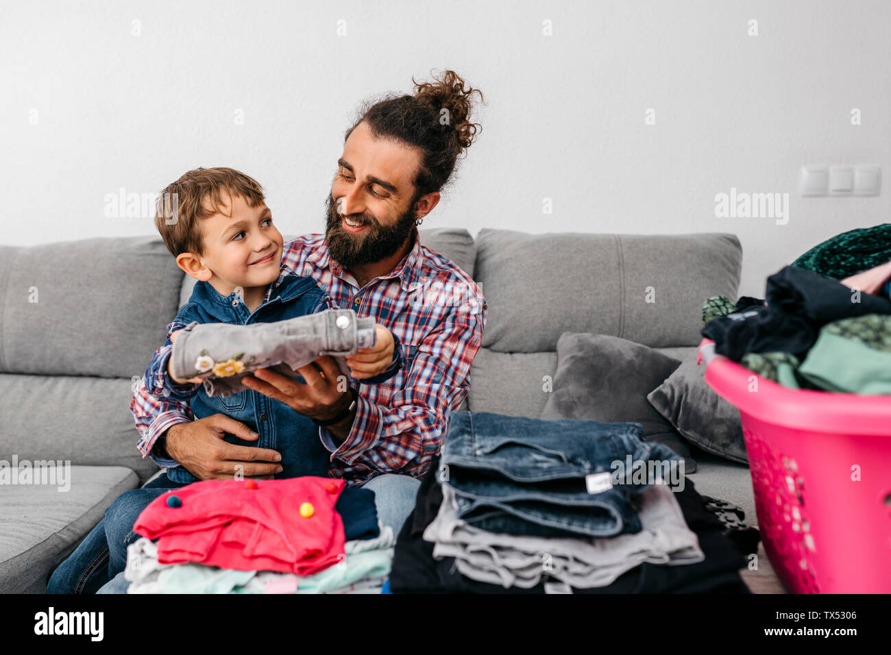 Ritratto di felice padre e figlio seduti insieme sul lettino la piegatura servizio lavanderia Foto Stock