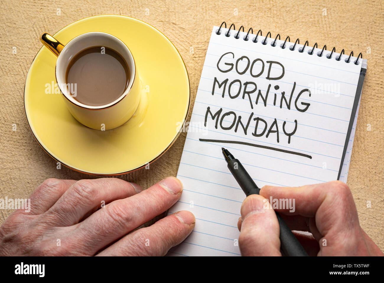 Buona mattina lunedì - man mano che scrive una nota con un pennarello nero in una spirale notebook, vista aerea con una tazza di caffè Foto Stock