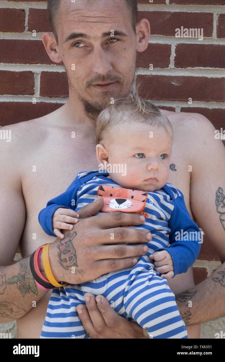 Un padre con tatuaggi tiene il suo Figlio bambino nelle braccia Foto Stock