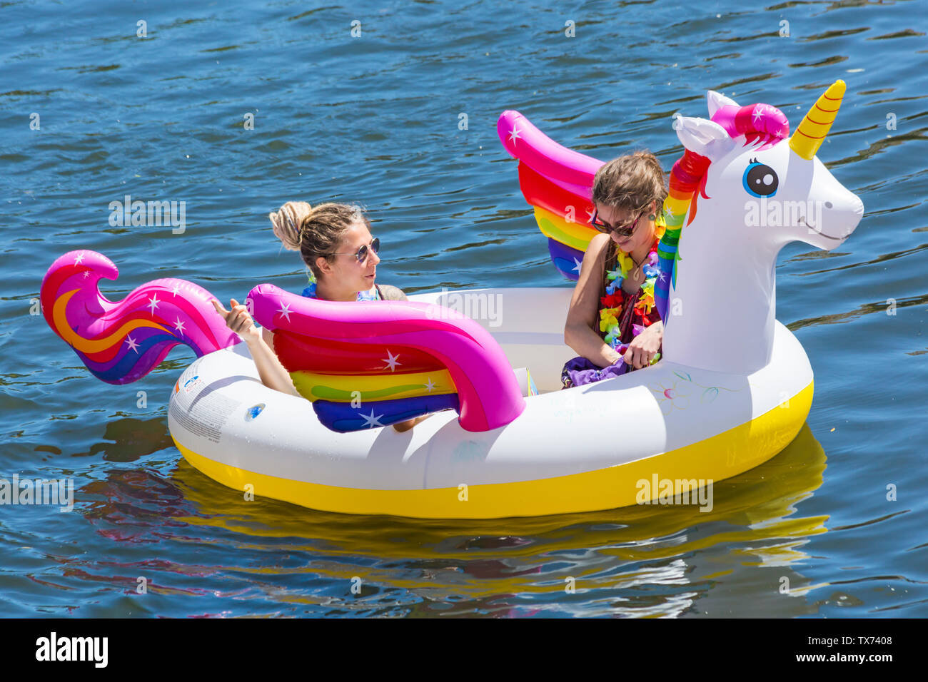 Due donne divertirsi sui gonfiabili gonfiabile unicorn su Dorset Dinghy giorno a Iford andando lungo il fiume Stour a Tuckton, Dorset Regno Unito nel mese di giugno Foto Stock