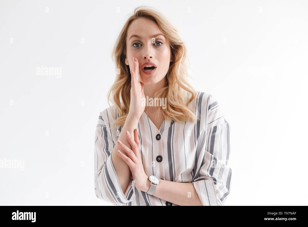 Ritratto di giovane donna bionda indossare orologi da polso gridando con la mano sulla sua bocca isolate su sfondo bianco in studio Foto Stock