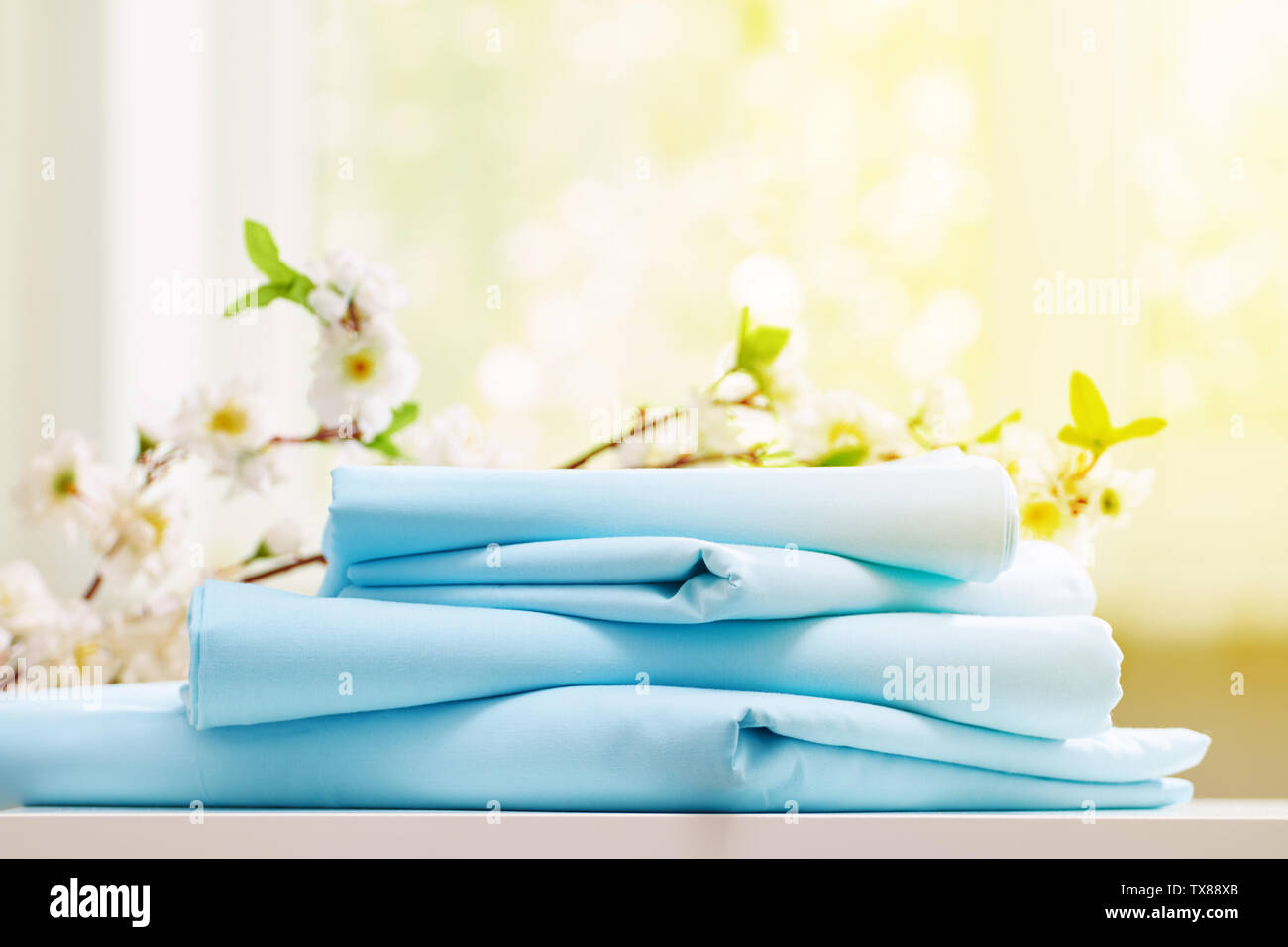 Closeup pila di blu biancheria da letto pulita su una cassettiera. Sfondo sfocato. La luce del sole dalla finestra. Foto Stock
