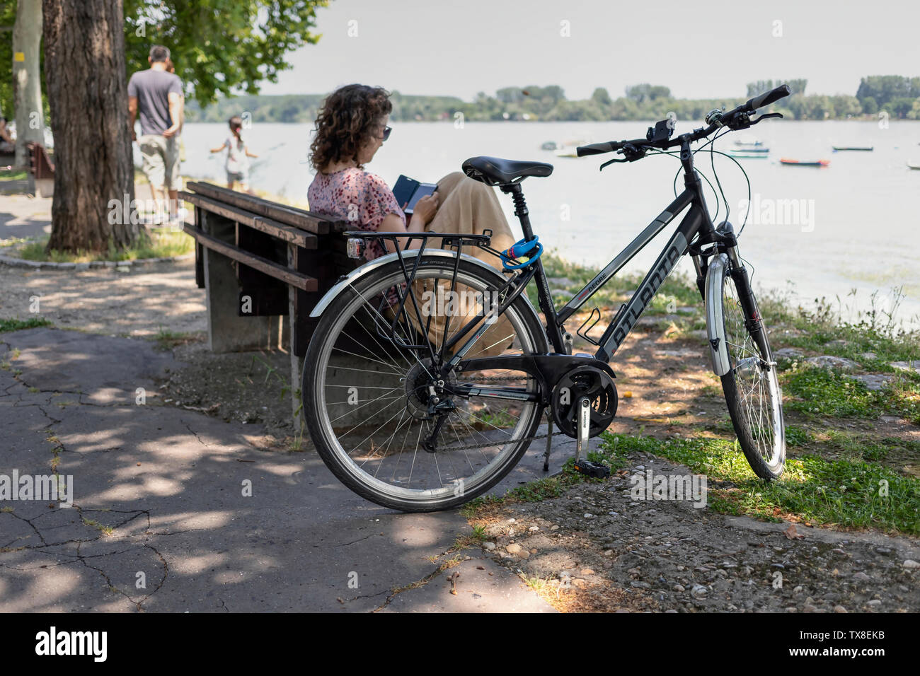 A Belgrado, in Serbia, 22 Giugno 2019: giovane donna seduta su una panchina accanto a una bicicletta parcheggiata presso il Danubio lungofiume a Zemun Foto Stock