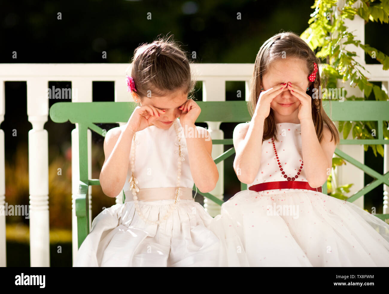 Due sorelle vestiti nei loro abiti di festa e cercando di non peek. Foto Stock