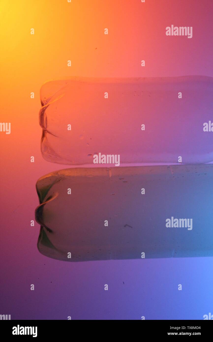 Close up di bottiglie trasparenti su uno sfondo colorato con illuminazione artificiale Foto Stock