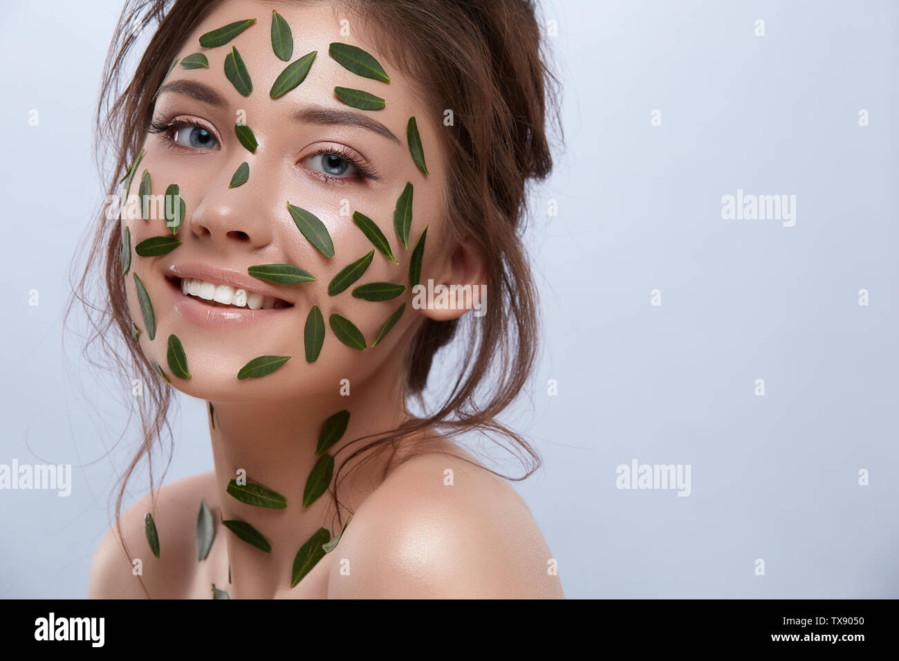 Felice ragazza con foglie verdi sul suo corpo sorridente alla telecamera, copia dello spazio naturale, beautiness, viso cura naturale Foto Stock