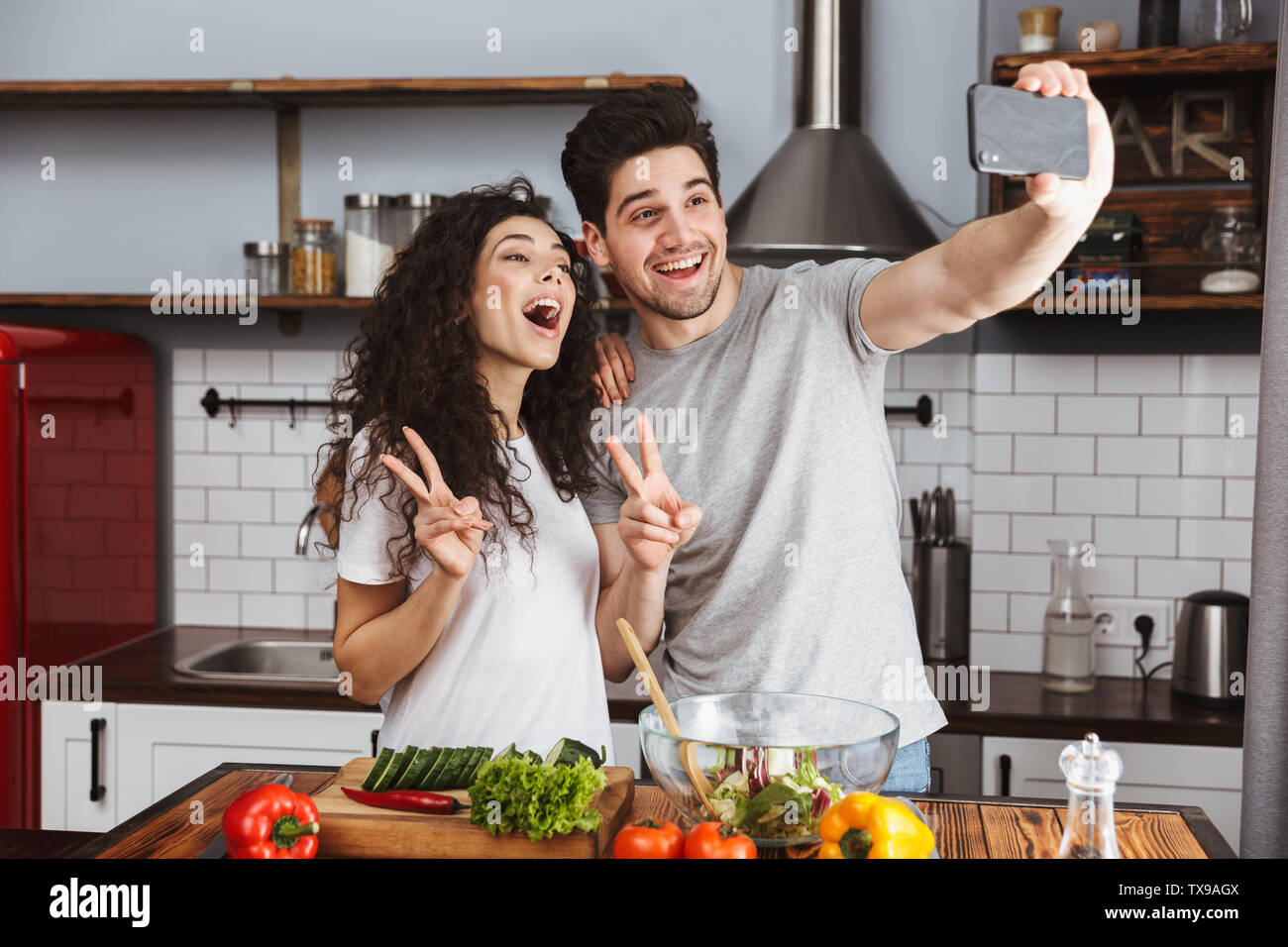 Foto di candida giovane uomo e donna 30s tenendo selfie foto durante la cottura salat con verdure insieme nella cucina moderna a casa Foto Stock