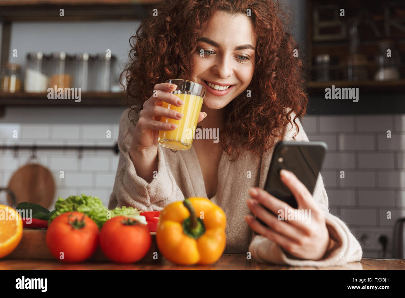 Immagine di tipo caucasico donna usando il cellulare mentre la cottura di verdura fresca insalata in cucina interna a home Foto Stock