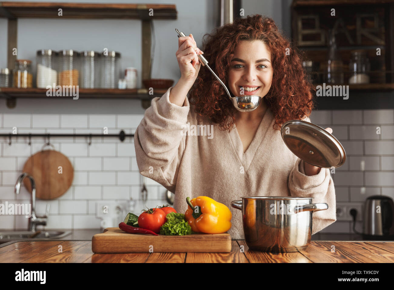 Foto di tipo caucasico donna tenendo la cottura cucchiaio siviera mentre mangia la minestra di verdure fresche in cucina a casa Foto Stock