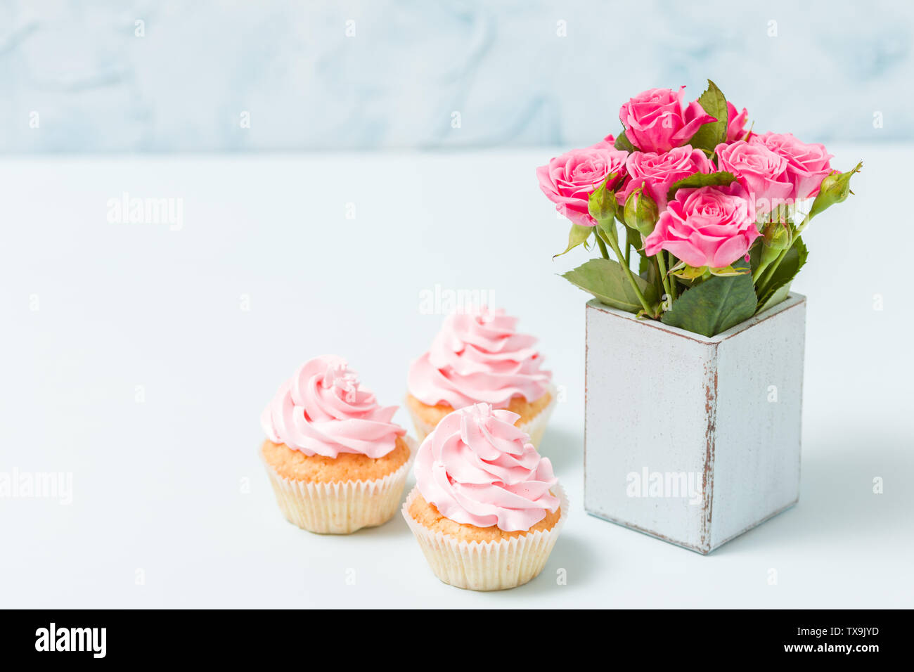 Tortina con crema rosa e Decorazione rose rosa in blu retrò shabby chic vaso. Pastello blu banner orizzontale con copia spazio per congratulazioni pos Foto Stock