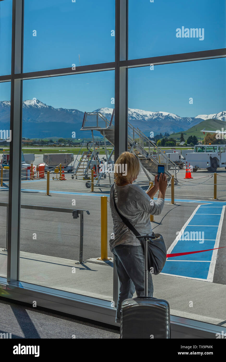 Donna con una valigia in aeroporto contro la finestra, Queenstown, New Zealand Nuova Zelanda. In verticale Foto Stock