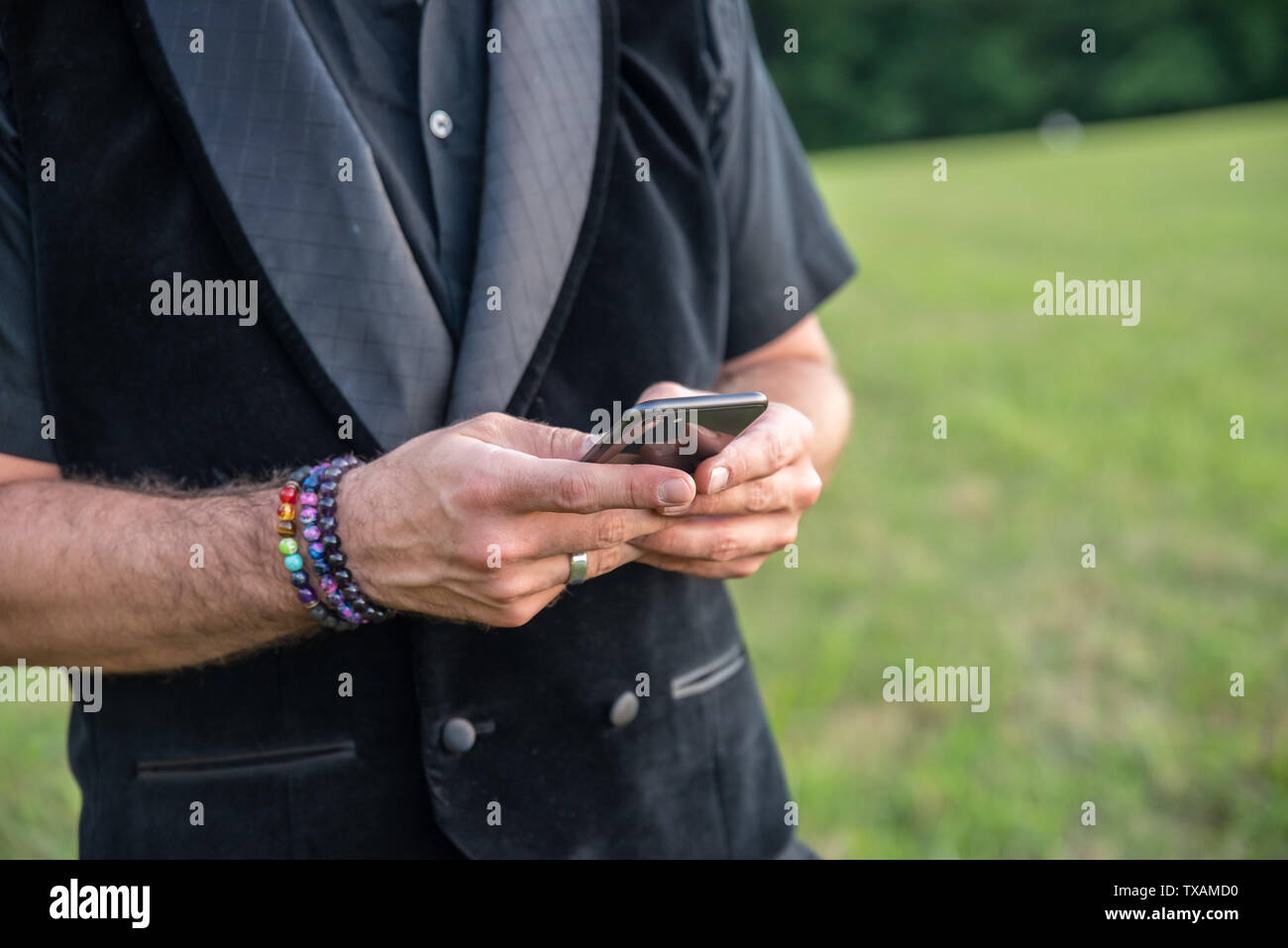 Alternativa sposato caucasion bianco uomo maschio in tutto nero e rainbow bracciali mentre i messaggi di testo sul suo telefono cellulare. Orgoglio per lgb, LGBT, o lgbtq. Foto Stock