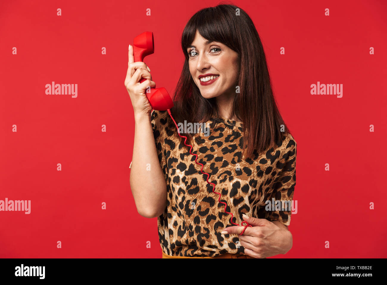 Immagine di una giovane e bella donna vestita di animale maglietta stampata in posa isolate su sfondo rosso parlando al telefono. Foto Stock