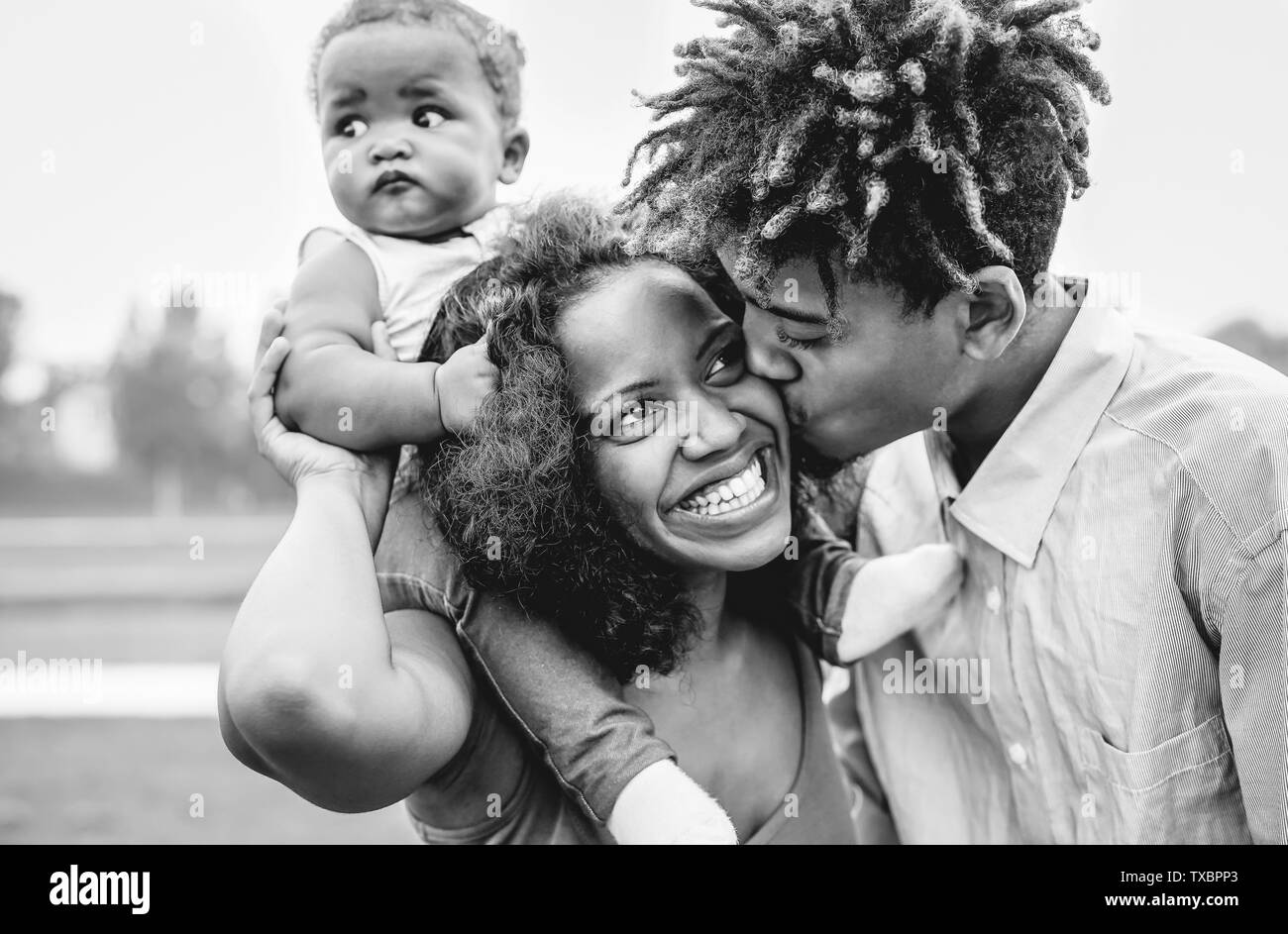 Felice famiglia africana divertirsi in un parco outdoor - il padre e la madre con la loro figlia godendo del tempo insieme in un giorno del fine settimana Foto Stock