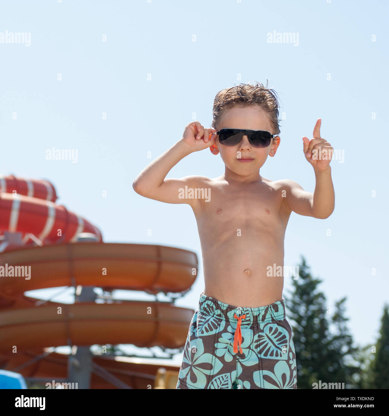 Bello piccolo felice ragazzo in occhiali da sole che mostra il numero uno con il dito in estate acqua park durante le vacanze Foto Stock
