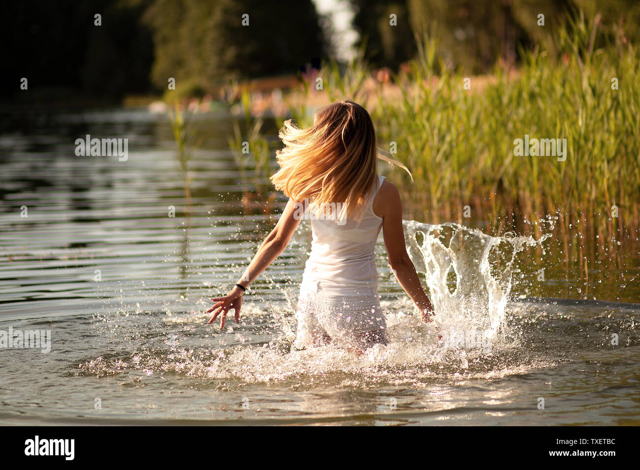 Snella ragazza con i capelli biondi dancing in acqua al tramonto e spruzzi d'acqua. Il concetto di libertà e di felicità, di amore. Foto Stock