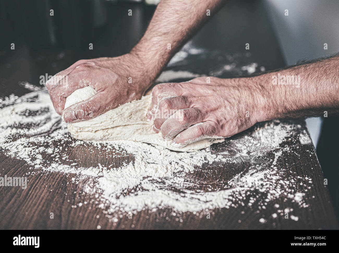 Close-up di mani di uomo impastare la pasta lievitata su infarinato e contatore di cucina Foto Stock