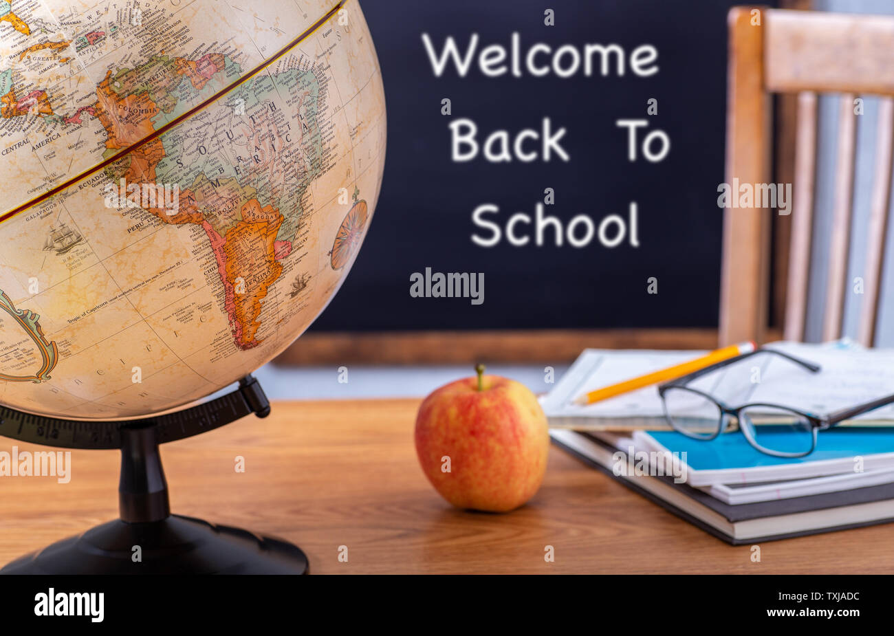 Primo piano di un globo su un banco di scuola con Benvenuti Torna a scuola scritti su una lavagna in background Foto Stock