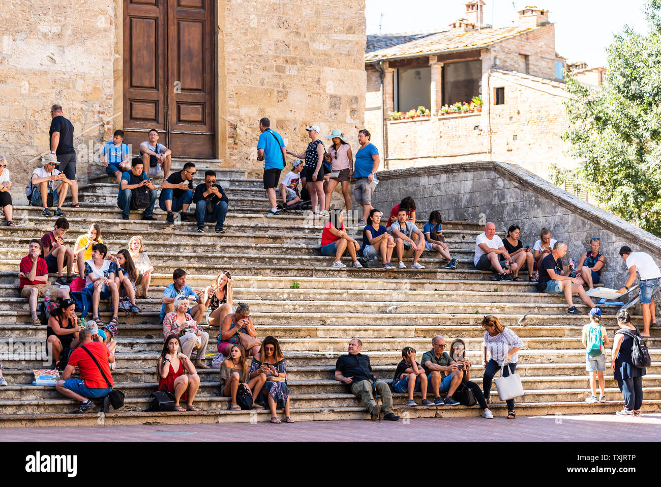 San Gimignano, Italia - 27 agosto 2018: persone sedute in appoggio sui gradini delle scale in piccola e antica città medievale Borgo in Toscana durante il giorno di estate Foto Stock