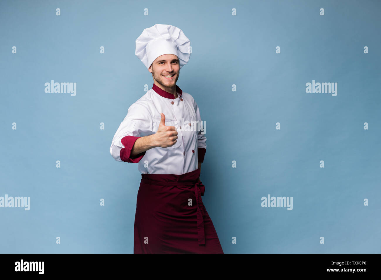 Immagine di felice giovane cuoco in uniforme che mostra pollice in alto Foto Stock