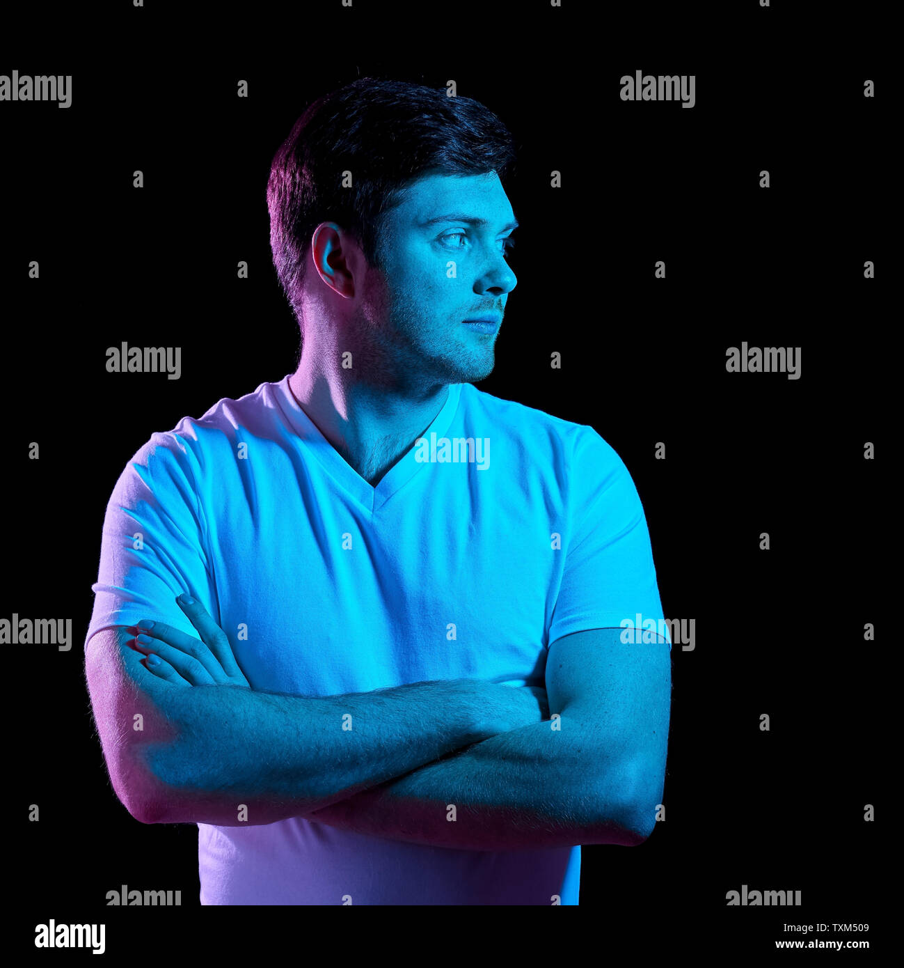 Uomo con bracci incrociati su luci al neon nelle tenebre Foto Stock