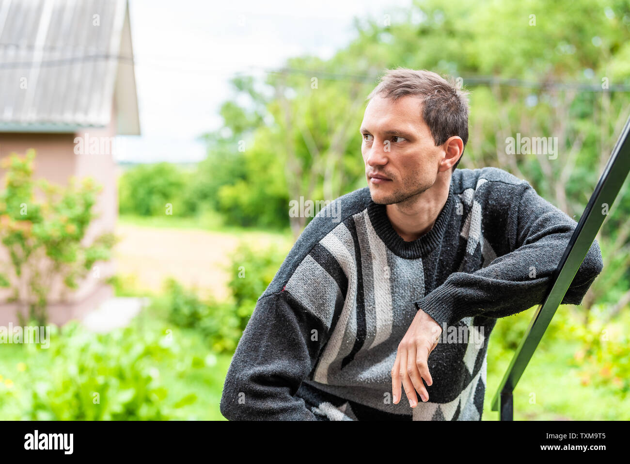 Giovane bello attraente uomo agricoltore closeup con stoppia in giardino verde estate ritratto di sfondo appoggiata sul parapetto Foto Stock