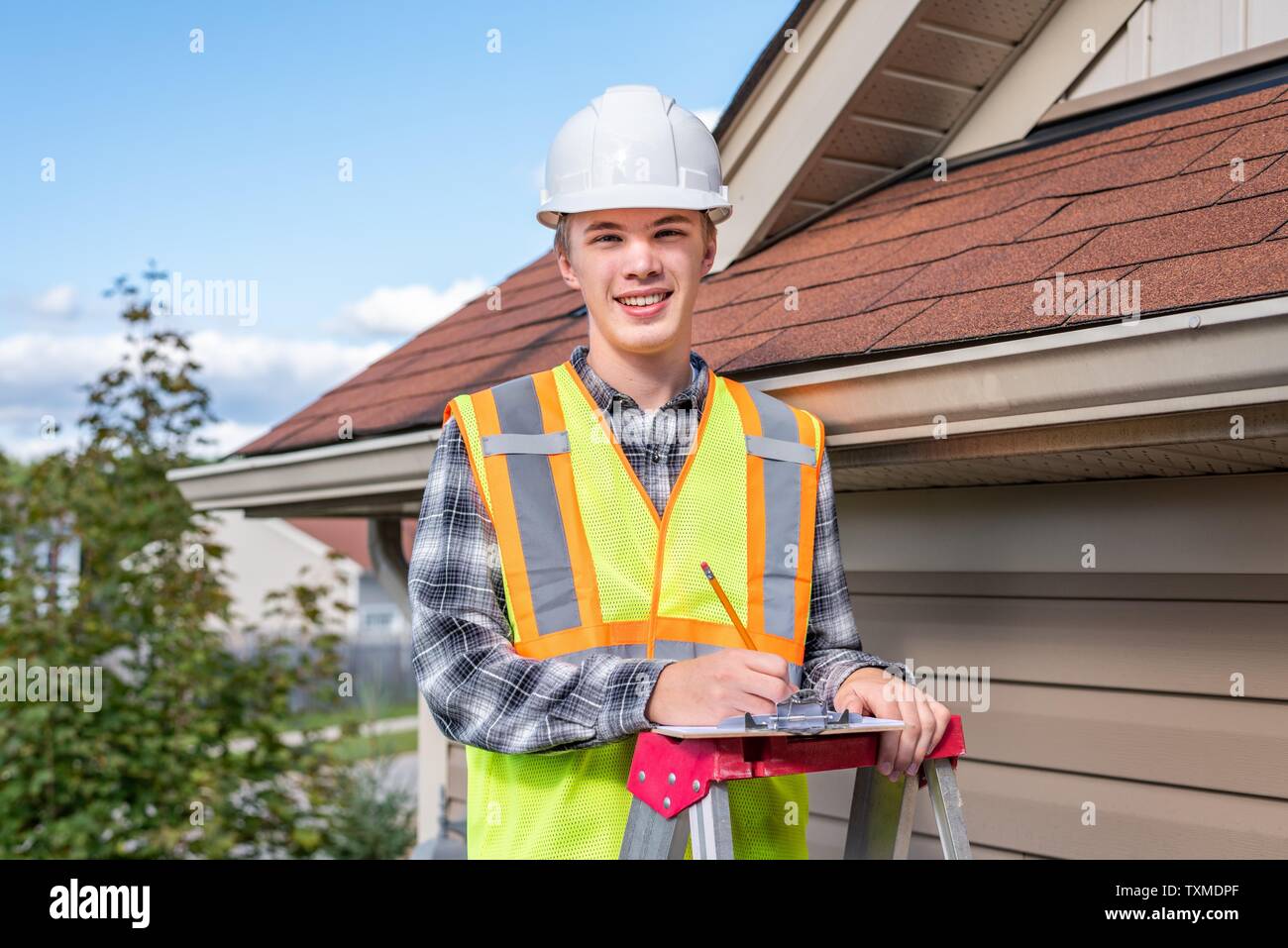 Home inspector in piedi su una scaletta e fornendo una ispezione al tetto di una casa. Foto Stock