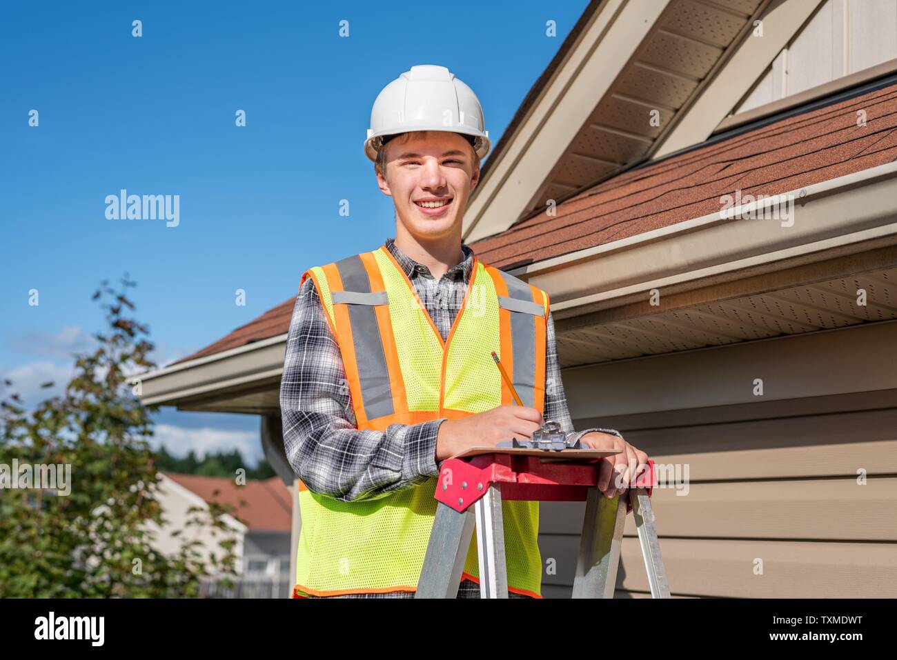 Home inspector in piedi su una scaletta e fornendo una ispezione al tetto di una casa. Foto Stock
