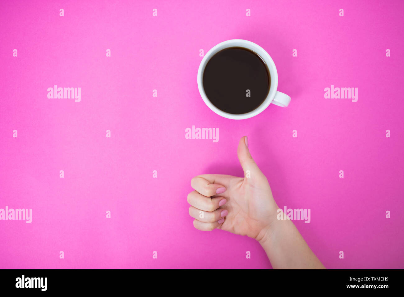 Flatlay con caffè nero in una tazza bianca. Donna che mostra a mano pollice in alto segno su un sfondo rosa. Foto Stock