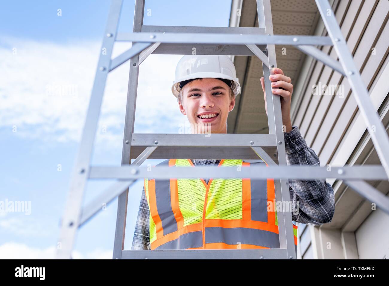 Giovane architetto maschio in piedi su una scaletta e vestito di ingranaggio di sicurezza. Foto Stock