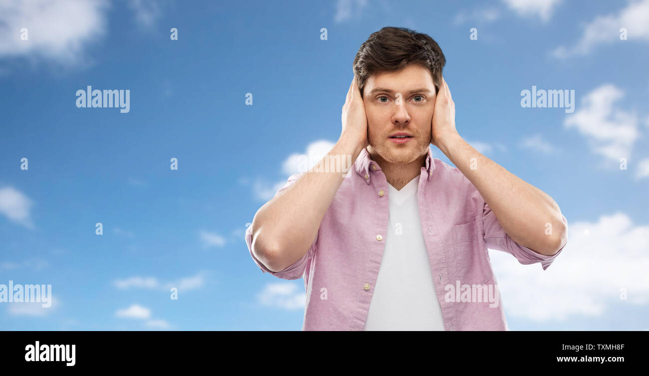 Uomo di chiudere le orecchie con le mani sul cielo blu Foto Stock