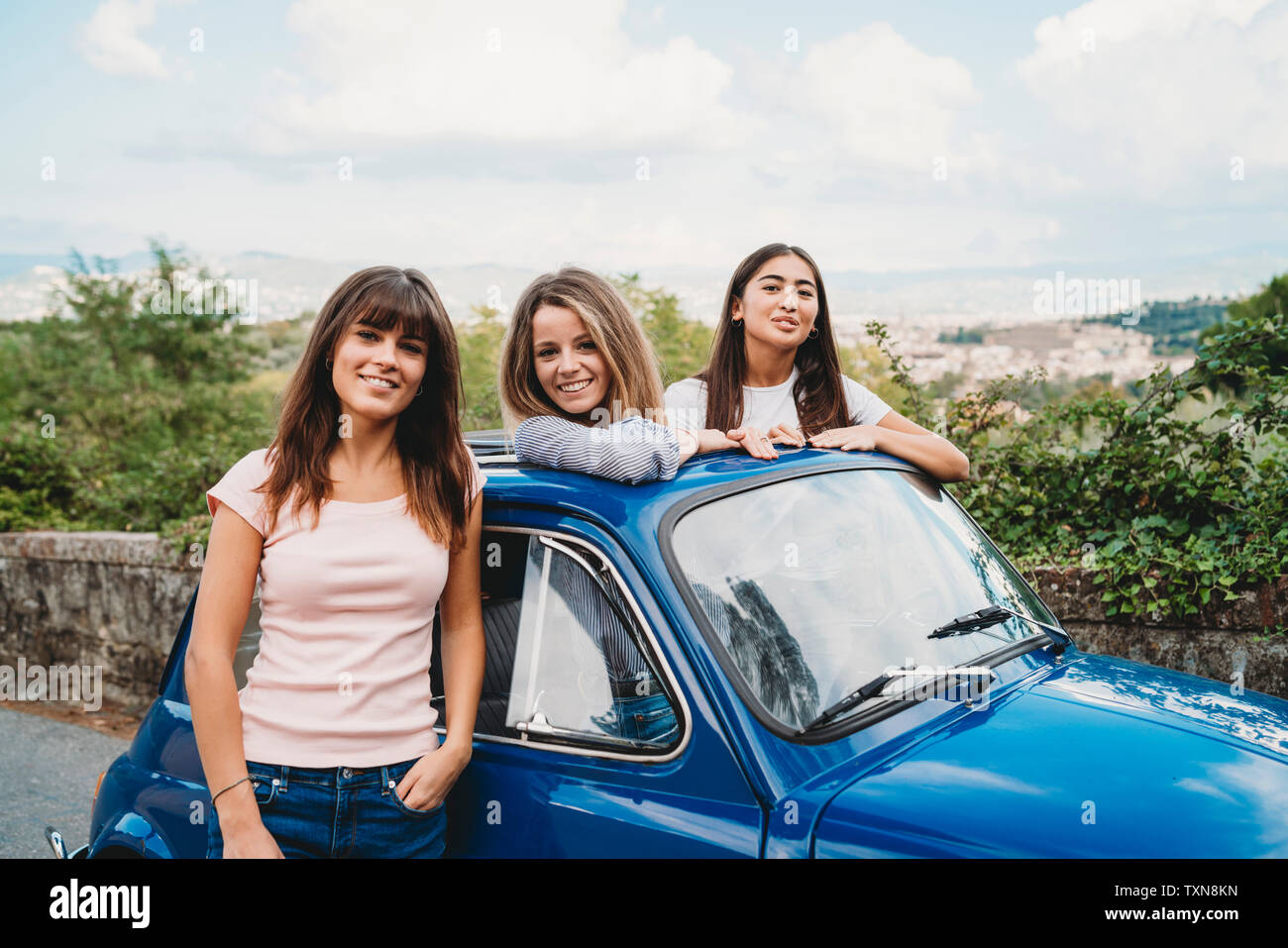 Donna in piedi accanto amici in posa di tettuccio apribile auto, Firenze, Toscana, Italia Foto Stock