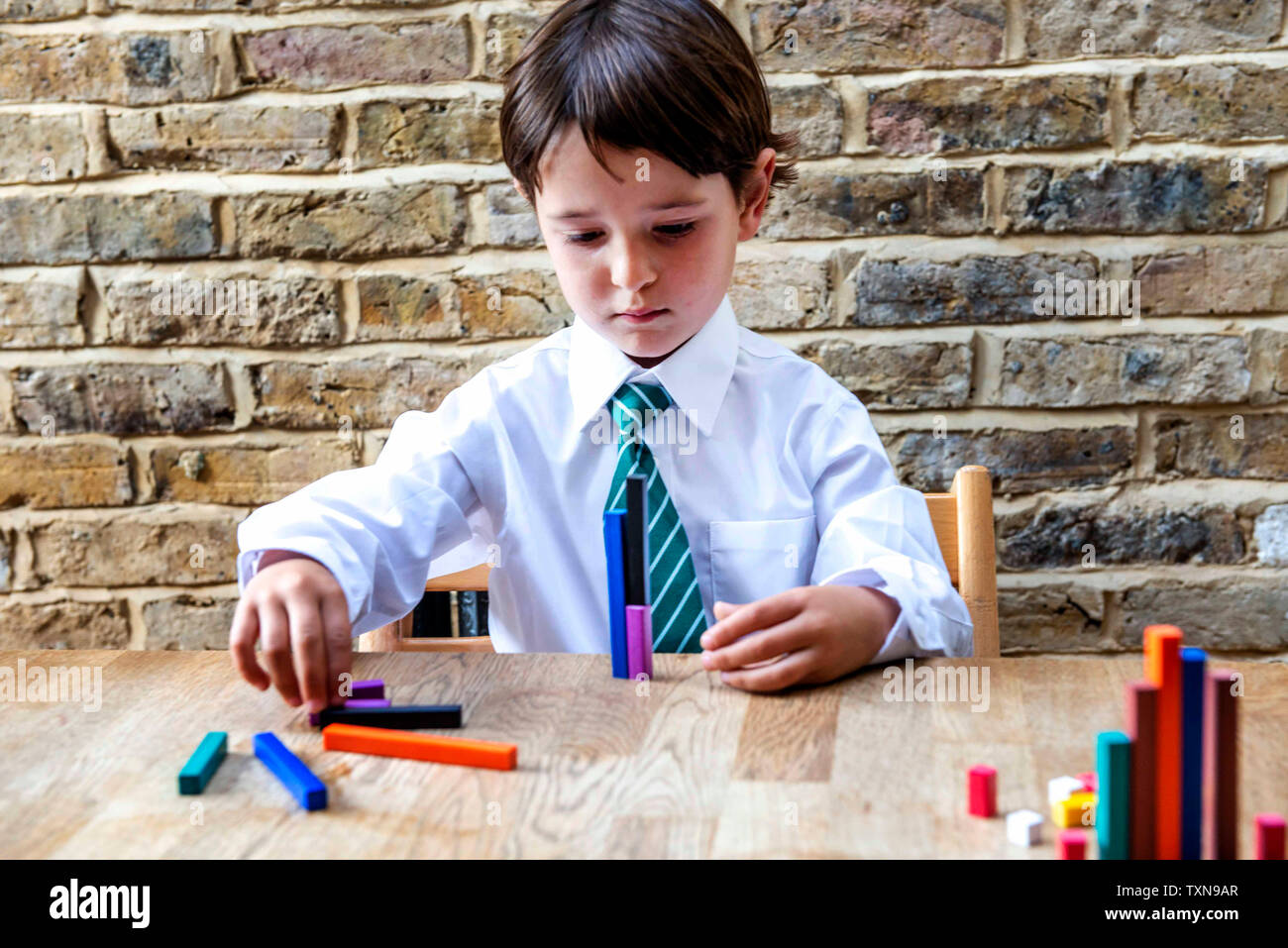 Ragazzo in uniforme scolastica a giocare con i colori bastoni a casa Foto Stock