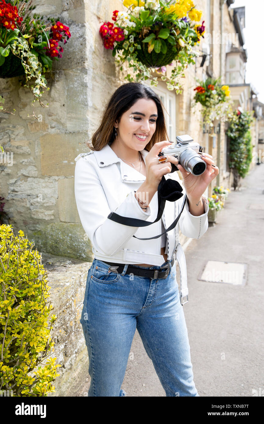 Giovane donna sulla strada del villaggio rivedendo le foto sulla fotocamera digitale, Cotswolds, Inghilterra Foto Stock