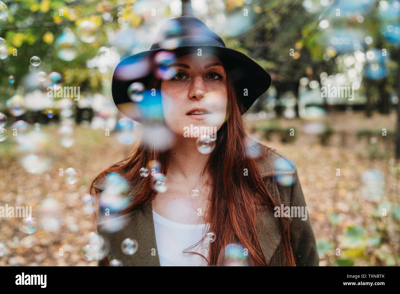 Giovane donna con lunghi capelli rossi tra le bolle galleggianti in autunno park, poco profondo ritratto di messa a fuoco Foto Stock