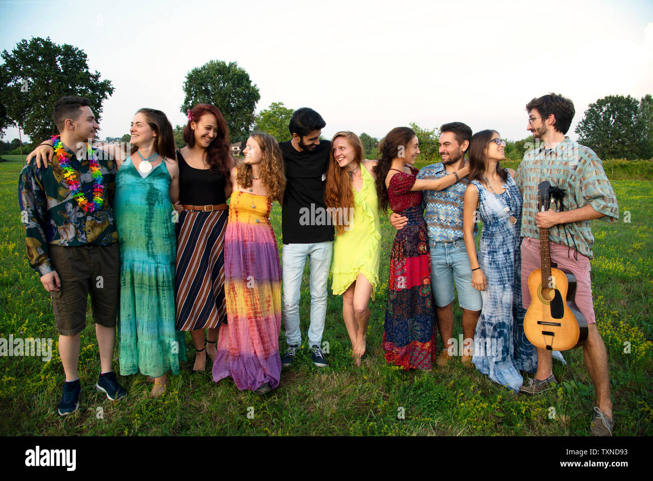 Grande gruppo di felice i giovani adulti in piedi in campo con le braccia intorno a ciascun altro Foto Stock
