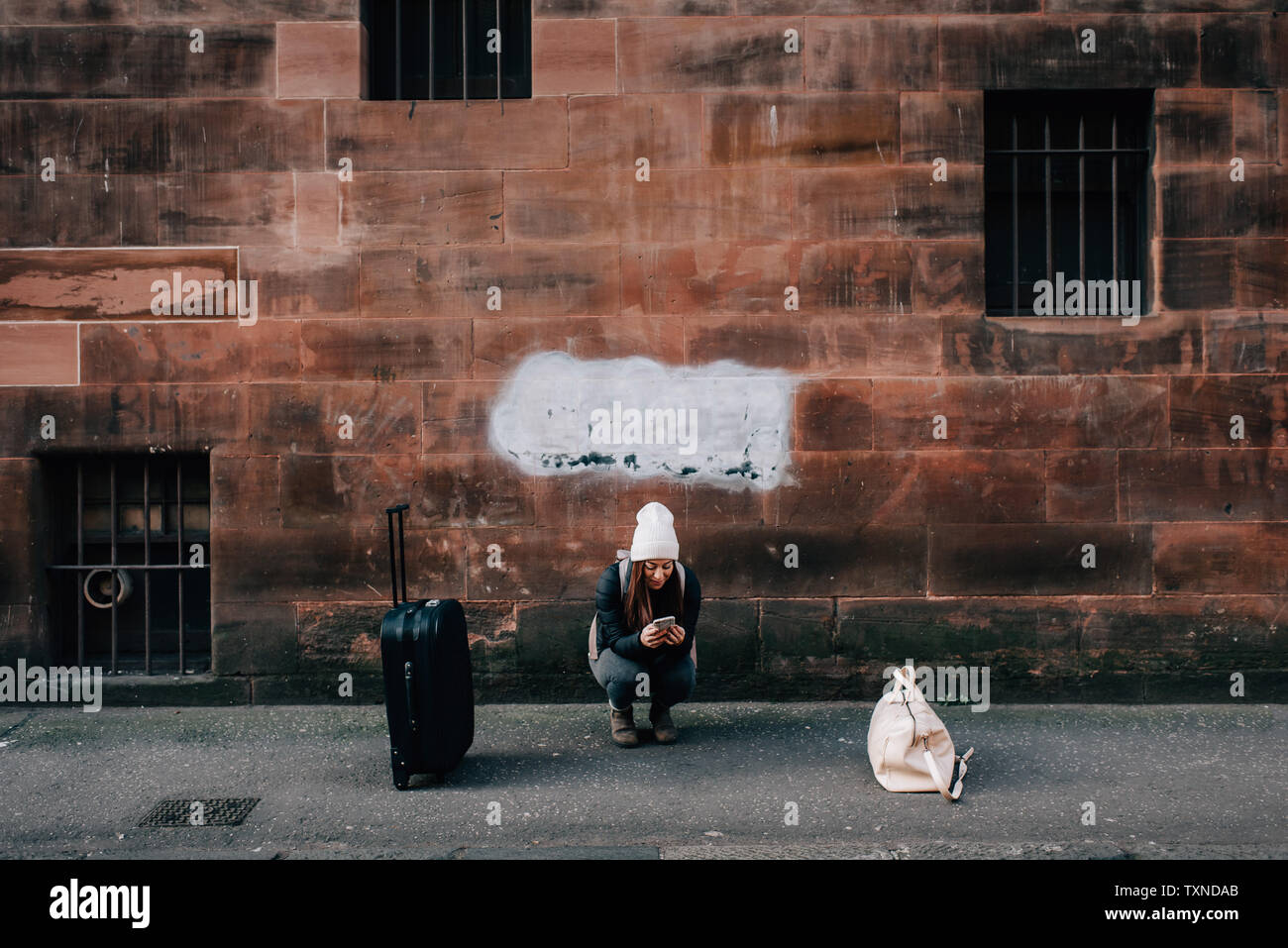 Donna texting sul cordolo con cellulare e bagagli, Edimburgo, Scozia Foto Stock