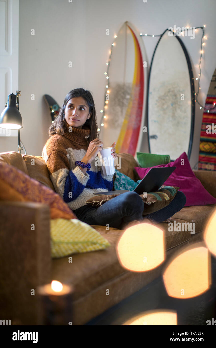 Giovane donna in maglia maglione rilassante sul divano con bevanda Foto Stock