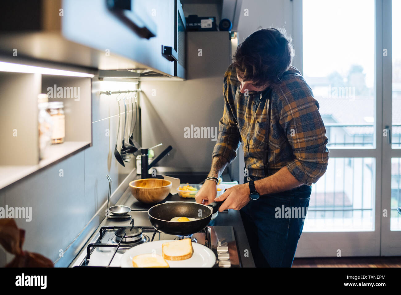 Metà uomo adulto preparare uova fritte al piano di cottura della cucina durante la chiamata sullo smartphone Foto Stock