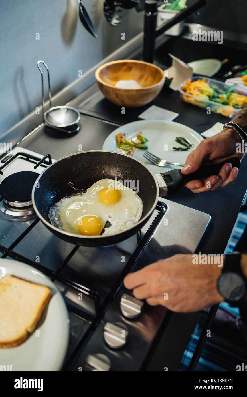 Metà uomo adulto preparare uova fritte al piano di cottura per cucina, ritagliato da vicino Foto Stock