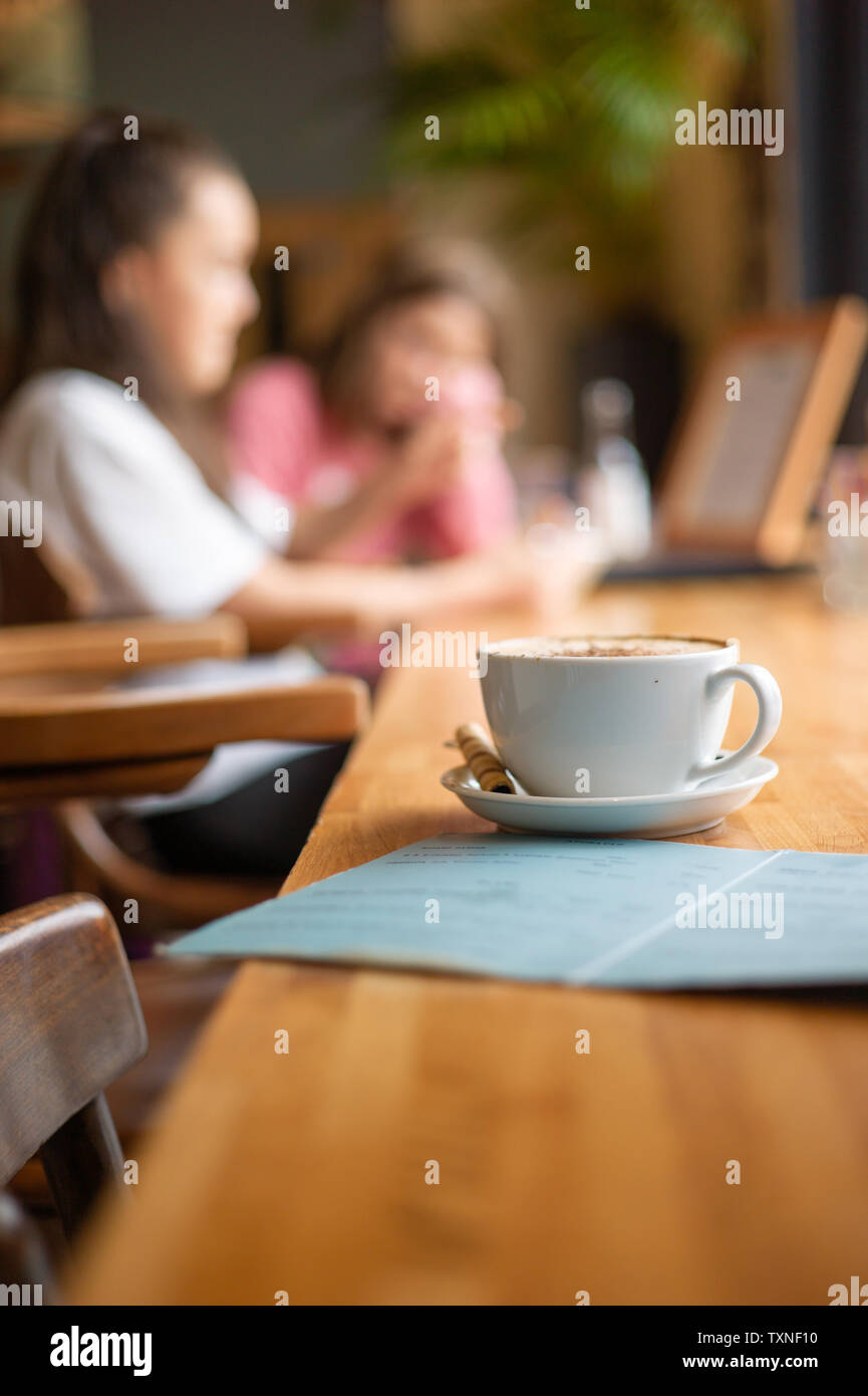 Una tazza di caffè e un menu con gente sullo sfondo ad un caffe' Francese Foto Stock