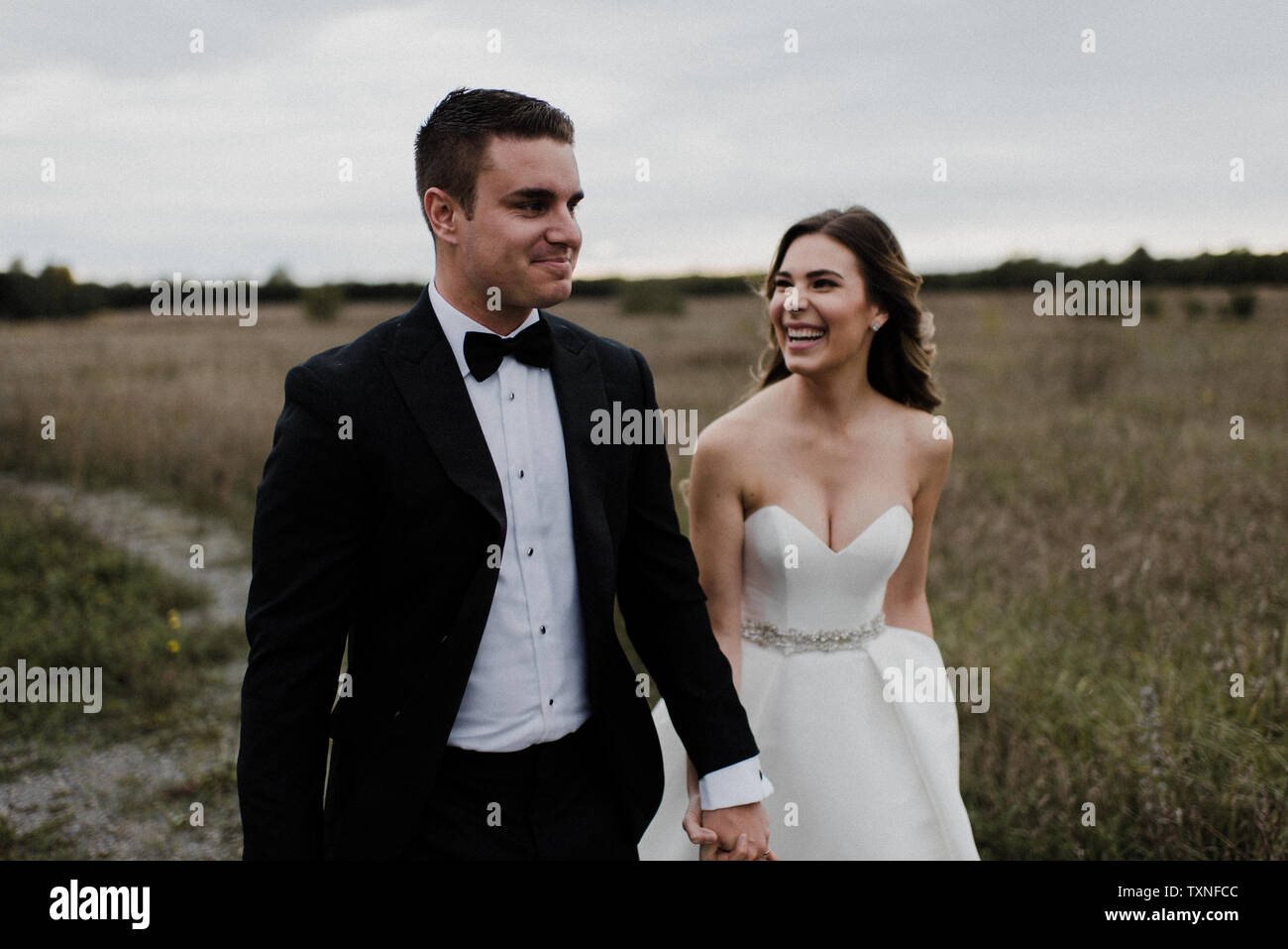 Felice coppia giovane passeggiando mano nella mano attraverso il campo sul giorno di nozze Foto Stock