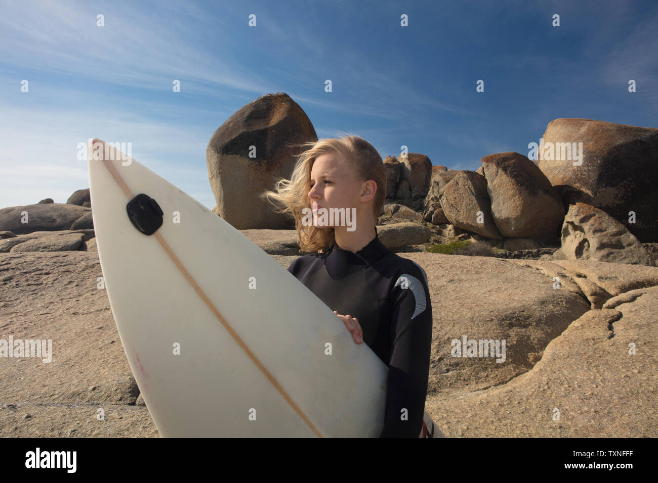 Giovani femmine surfer con capelli oltremare guardando fuori dalla spiaggia rock, Cape Town, Western Cape, Sud Africa Foto Stock