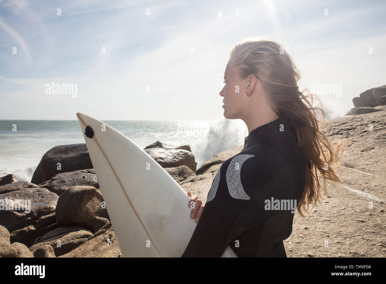 Giovani femmine surfer con capelli oltremare guardando fuori dalla spiaggia rock, Cape Town, Western Cape, Sud Africa Foto Stock