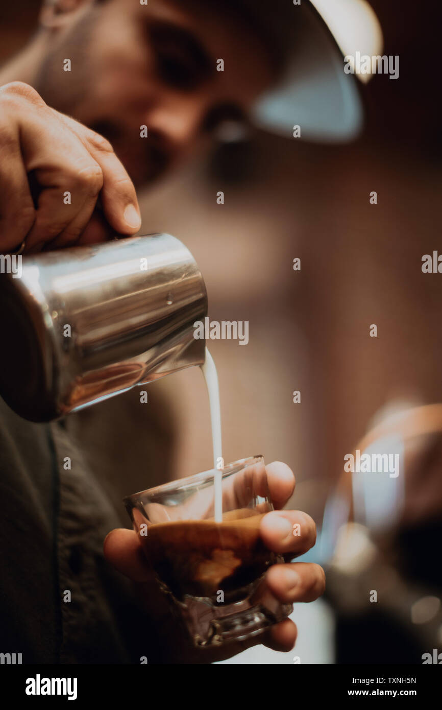 Barista versando il latte nel caffè di vetro in cafe, close up delle mani Foto Stock