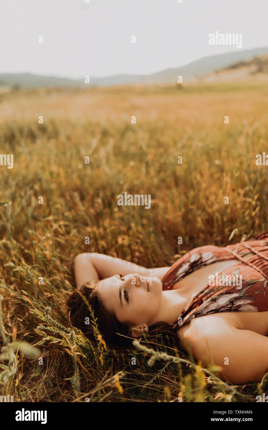 Bella giovane donna guardando in alto mentre giaceva nel campo di erba lunga, Exeter, CALIFORNIA, STATI UNITI D'AMERICA Foto Stock