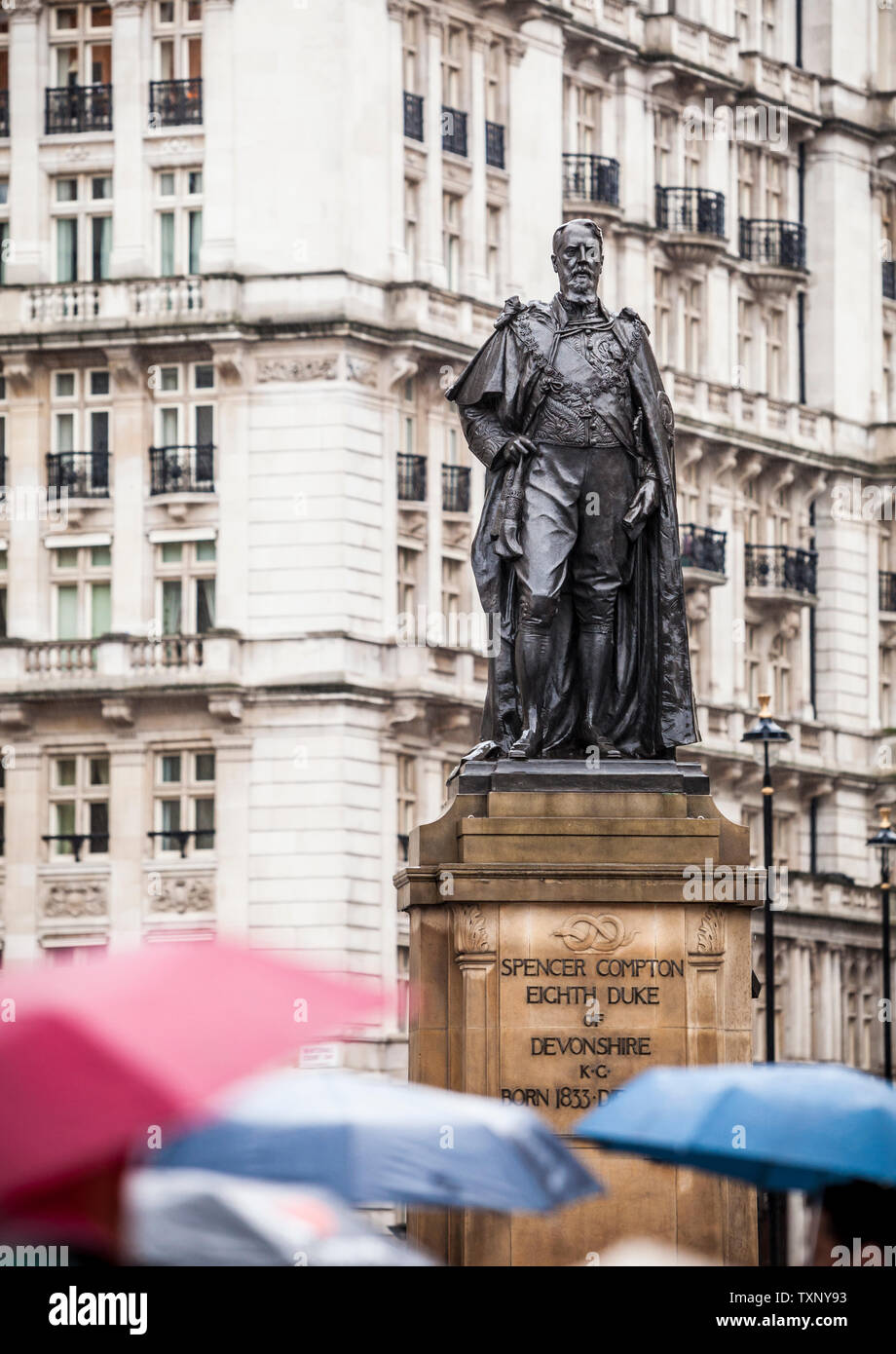 Persone ombrelli azienda a piedi passato la statua del duca di Devonshire, Horse Guards Ave, Whitehall, Westminster, London, Regno Unito. Foto Stock