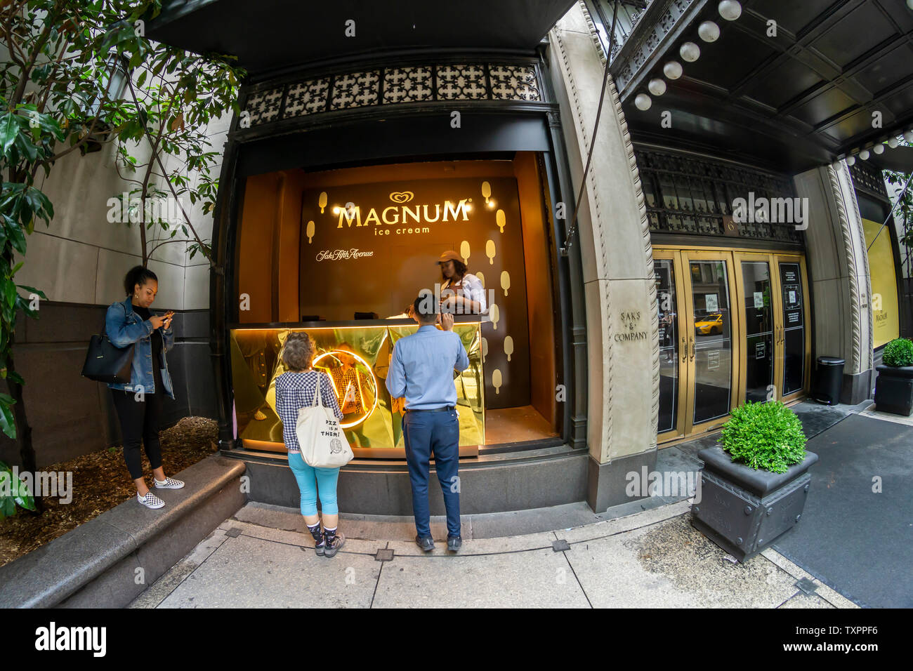 Ice Cream amanti passo fino a una finestra di Saks Fifth Avenue a New York che ha il vetro rimosso e viene rimodellata in un "Ice Cream Parlor" per il buon umore Co. Magnum del mini-bar give-away Martedì, 18 giugno 2019. Magnum, che è una marca di buon umore, che di per sé è di proprietà del conglomerato gigante Unilever, regalato Magnum Mini Bar Gelateria prodotti in vari gusti nel caso di branding. (© Richard B. Levine) Foto Stock