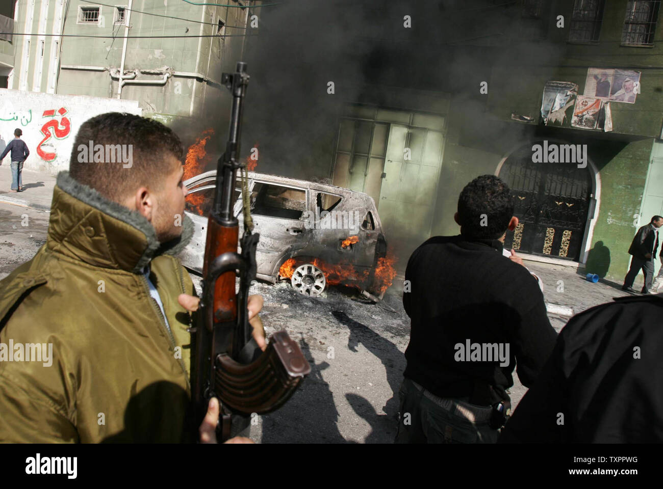 Un palestinese pistolero sorge accanto alla bruciata veicoli, nella città di Gaza, nella Striscia di Gaza il 20 dicembre 2006. I veicoli sono stati dati alle fiamme dai parenti dei due pro-Fatah militanti che sono stati uccisi martedì durante gli scontri con miliziani di Hamas solo poche ore dopo una tregua ha preso effetto. (UPI foto/Ismael Mohamad) Foto Stock