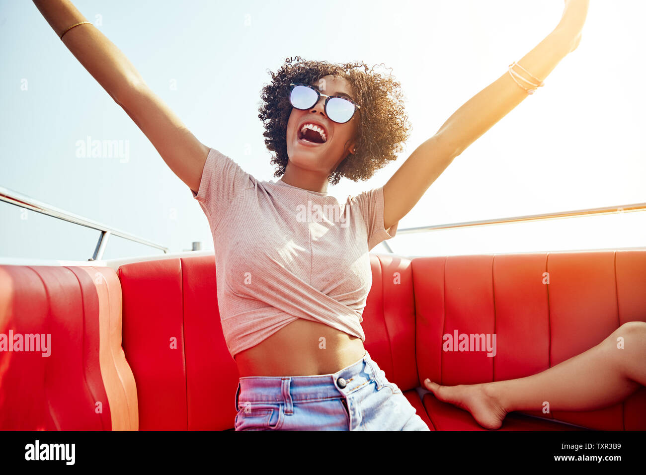 Giovane donna di ridere mentre è seduto su una barca con le braccia sollevate in aria durante le sue vacanze estive Foto Stock